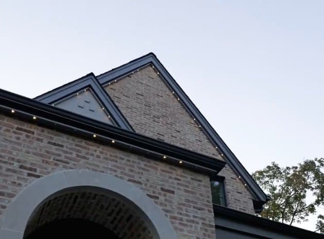 Close-up of the Naperville home's gable roofline at dusk, permanent light fixtures barely visible against the black trim