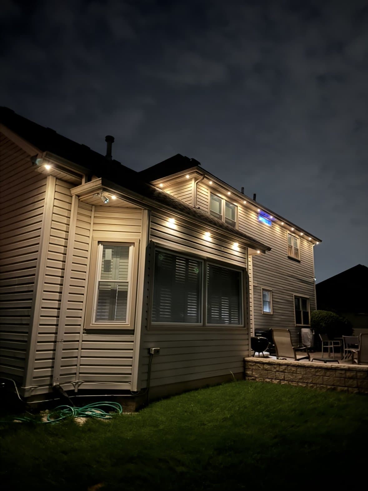 Back of the Plainfield home lit in warm white along the roofline above the patio